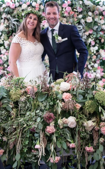 Brudepar foran en blomstervegg i rosa og grønt