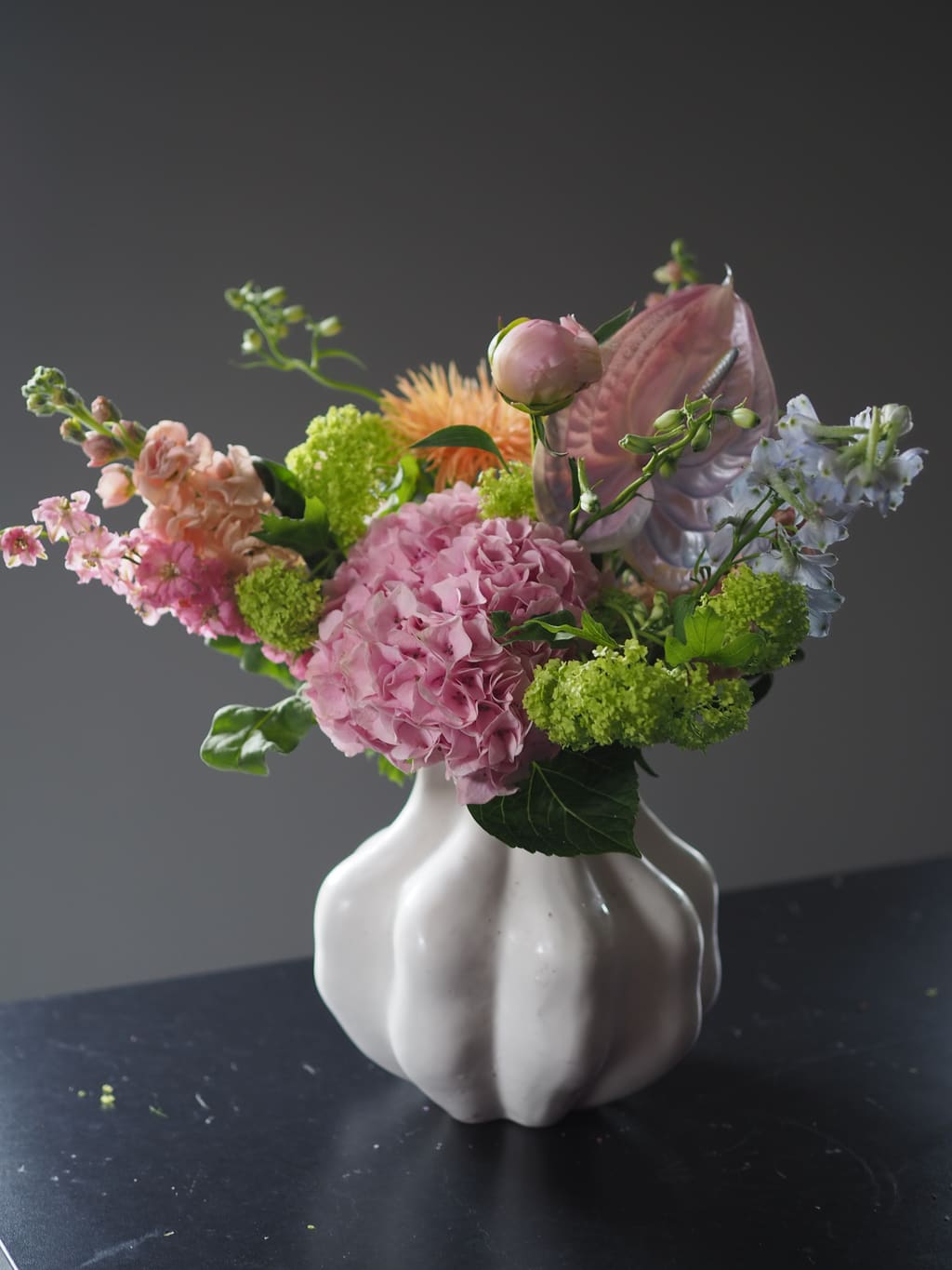 Blomsteroppsats i rosa og grønt i en hvit, bølget keramikkvase.