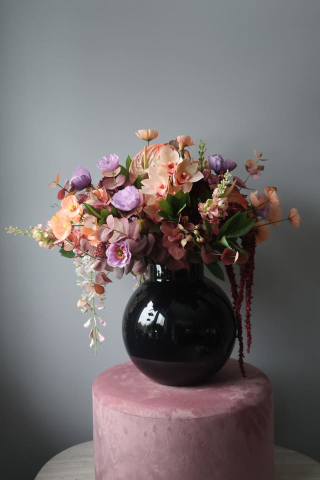 Blomsteroppsats i sort vase på en rosa krakk.